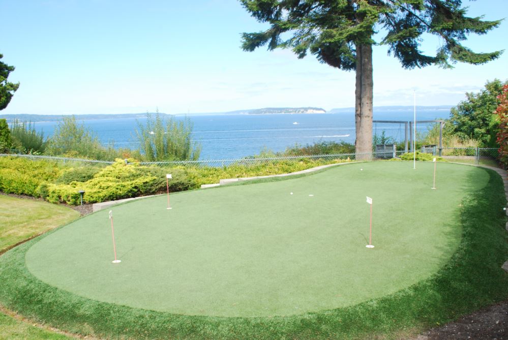 Spacious backyard putting greens installed with premium artificial turf, featuring multiple practice cups and flagsticks, set against a scenic landscape for realistic at-home golf practice.