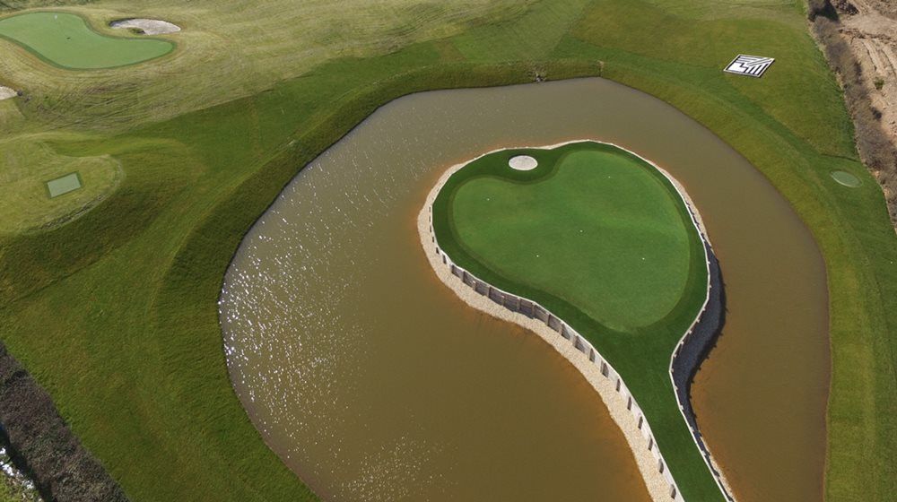 Metro New York Aerial view of a vibrant green synthetic grass island in a natural pond on a golf course