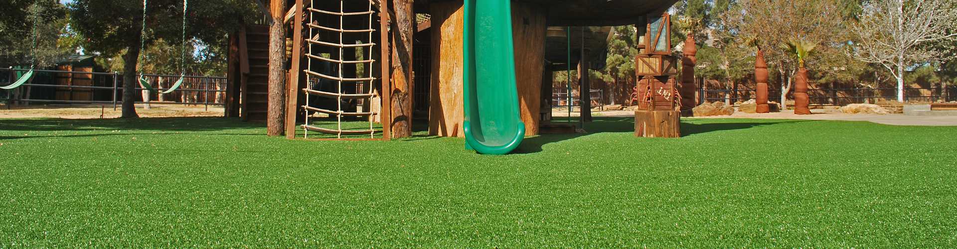 Child-safe synthetic turf playground surface installed under wood play structure with slide
